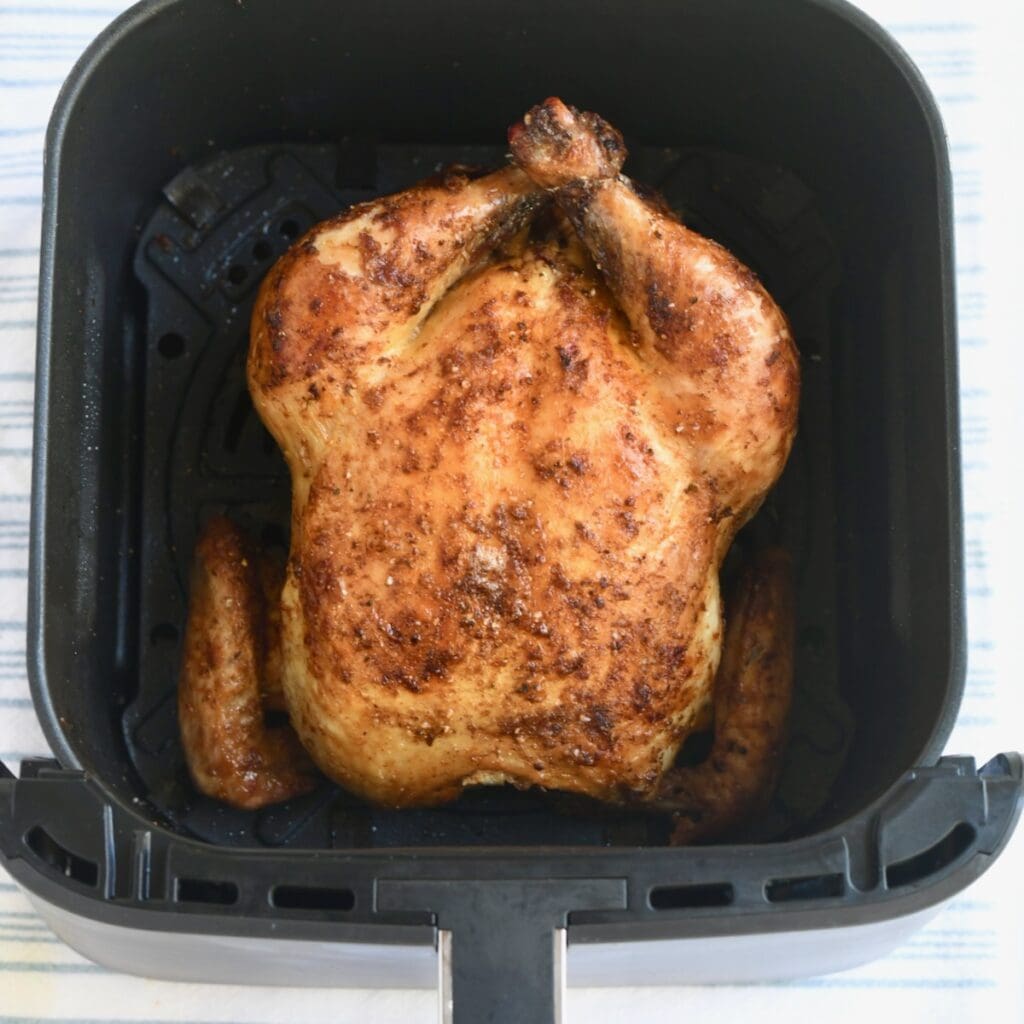 A whole roasted chicken in an air fryer basket.
