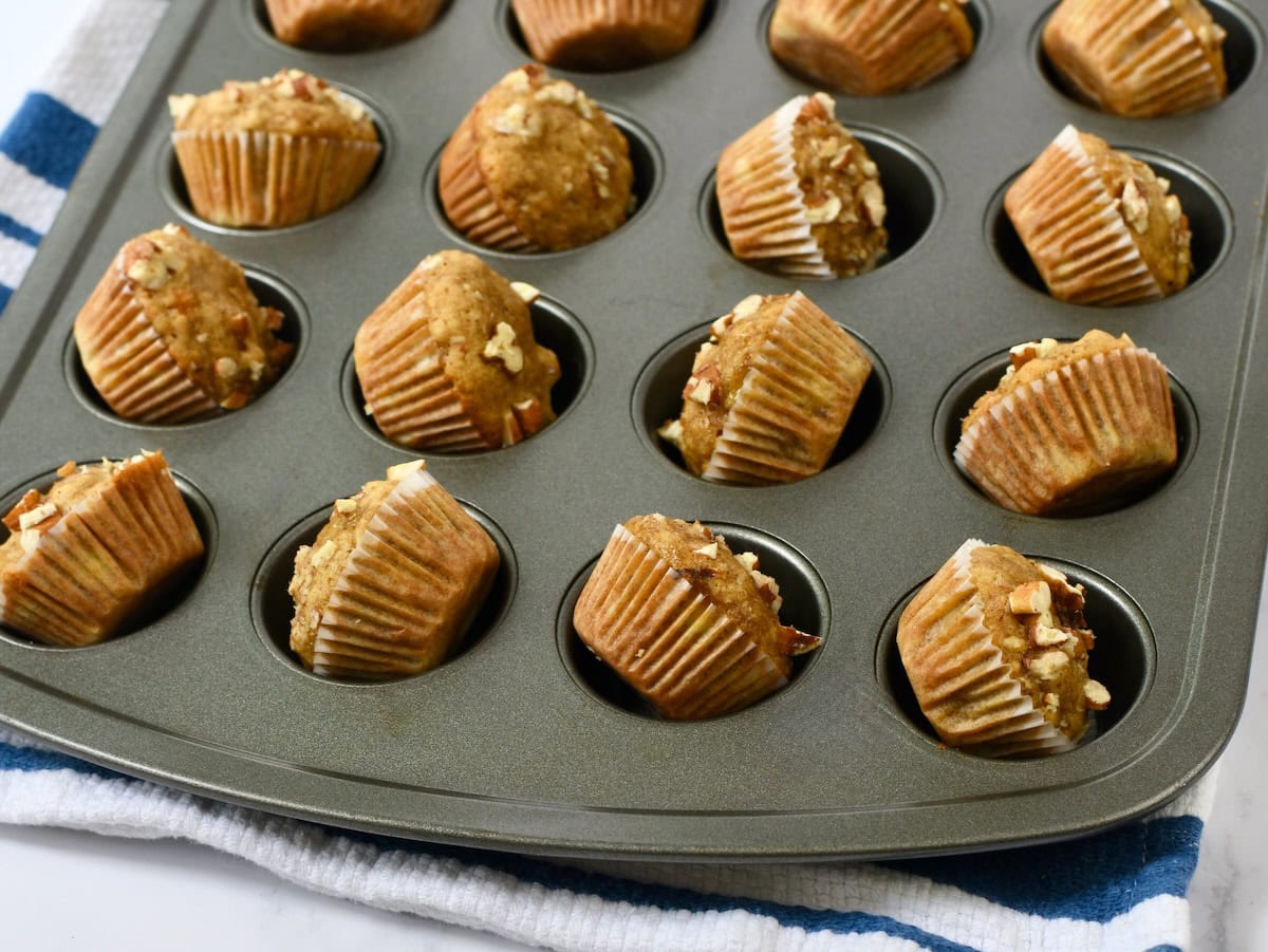 Mini banana muffins tipped on the side in the muffin pan to cool.