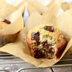 Bakery style chocolate chunk banana muffins in brown parchment liners and bite taken out.