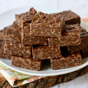 Peanut butter chocolate rice crispy treat bars stacked on white plate on wood slab.
