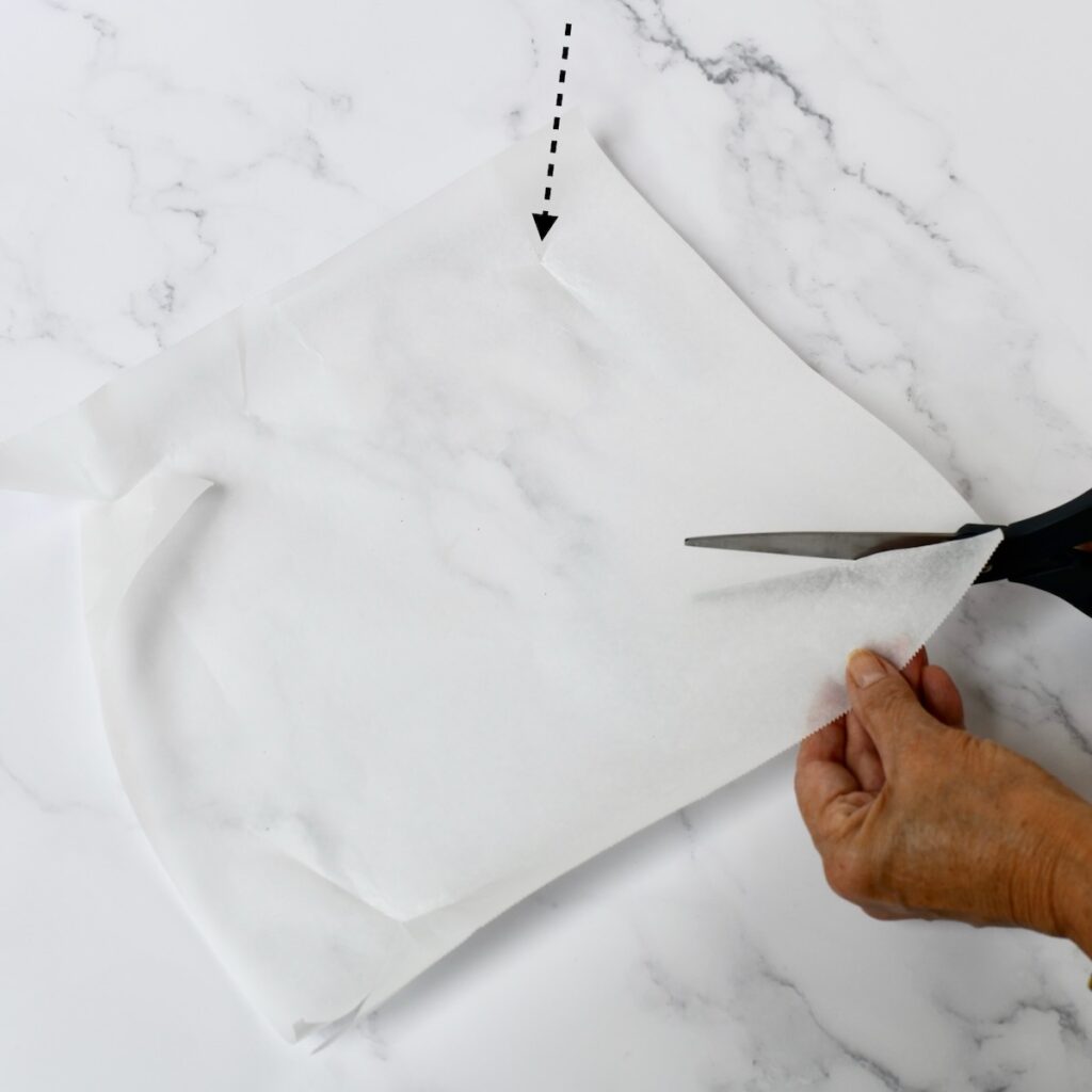 Scissors cutting into the corner of a square of parchment to line a pan with.
