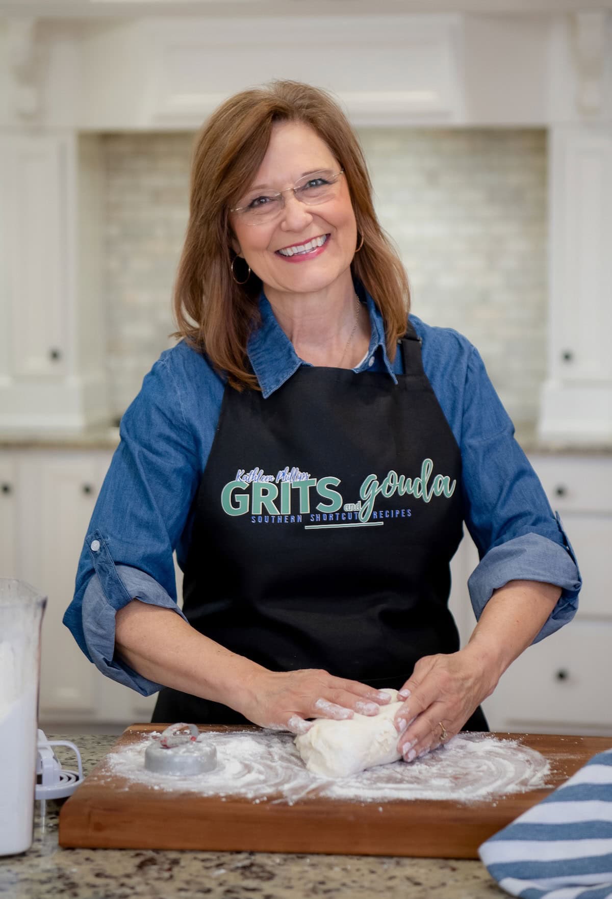 Woman, Kathleen Phillips, with apron on that says Grits and Gouda, kneading biscuit dough.