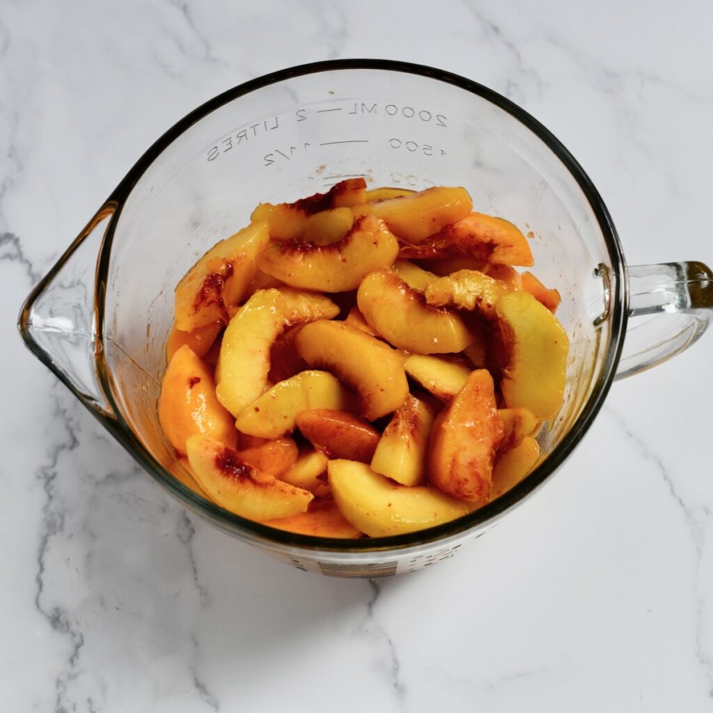 Fresh peach slices in a glass measuring bowl.