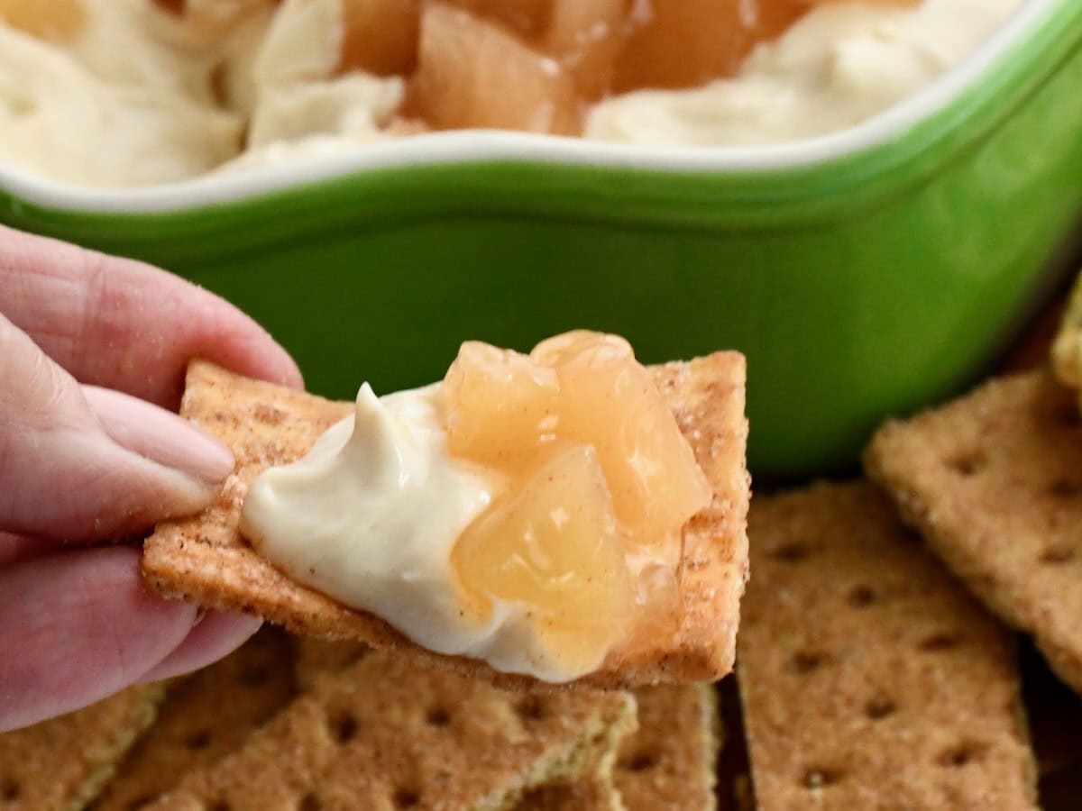 Hand holding a graham cracker topped with apple pie dip and apple filling