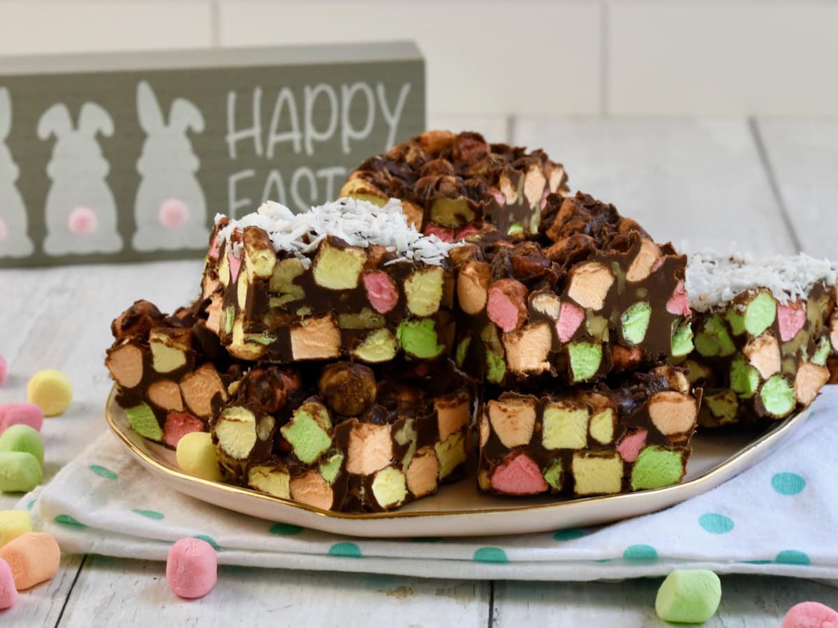 chocolate cathedral window bars with colorful mini marshmallows stacked on a plate, easter sign in the background