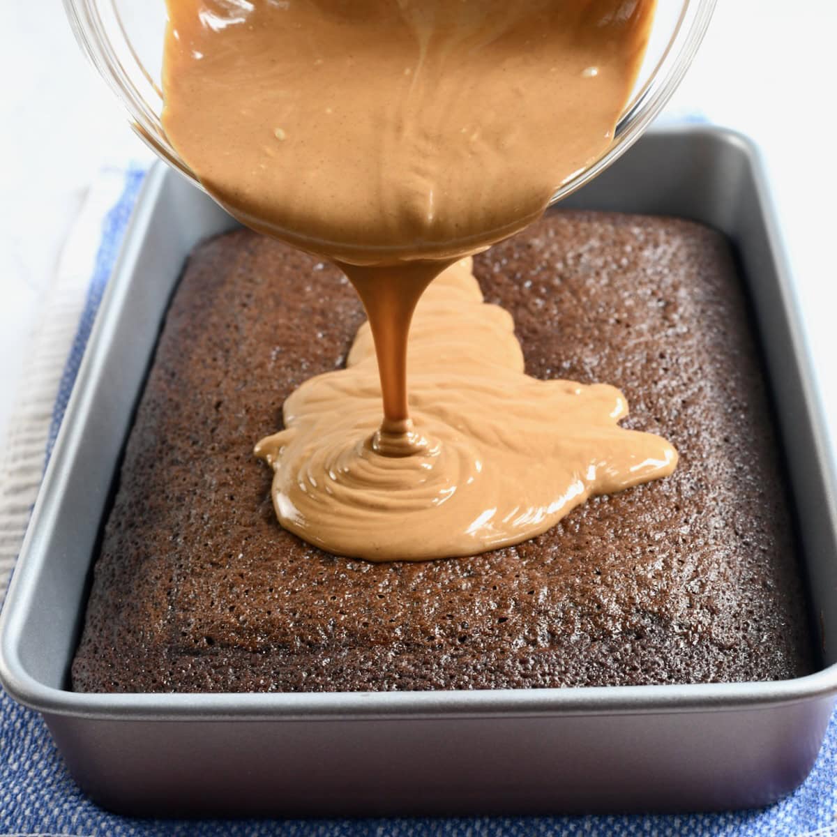 Pouring peanut butter layer over baked chocolate cake in a 9x13 pan