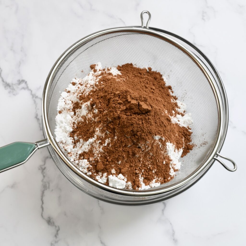 Sifting cocoa powder and powdered sugar into a bowl