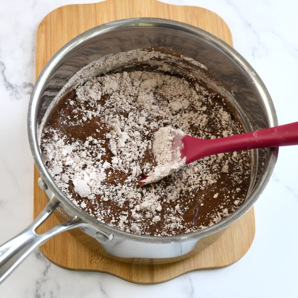 Stirring powdered sugar into melted chocolate frosting mixture in a saucepan