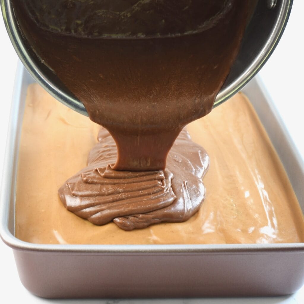 Pouring chocolate frosting over the peanut butter layer on a sheet cake