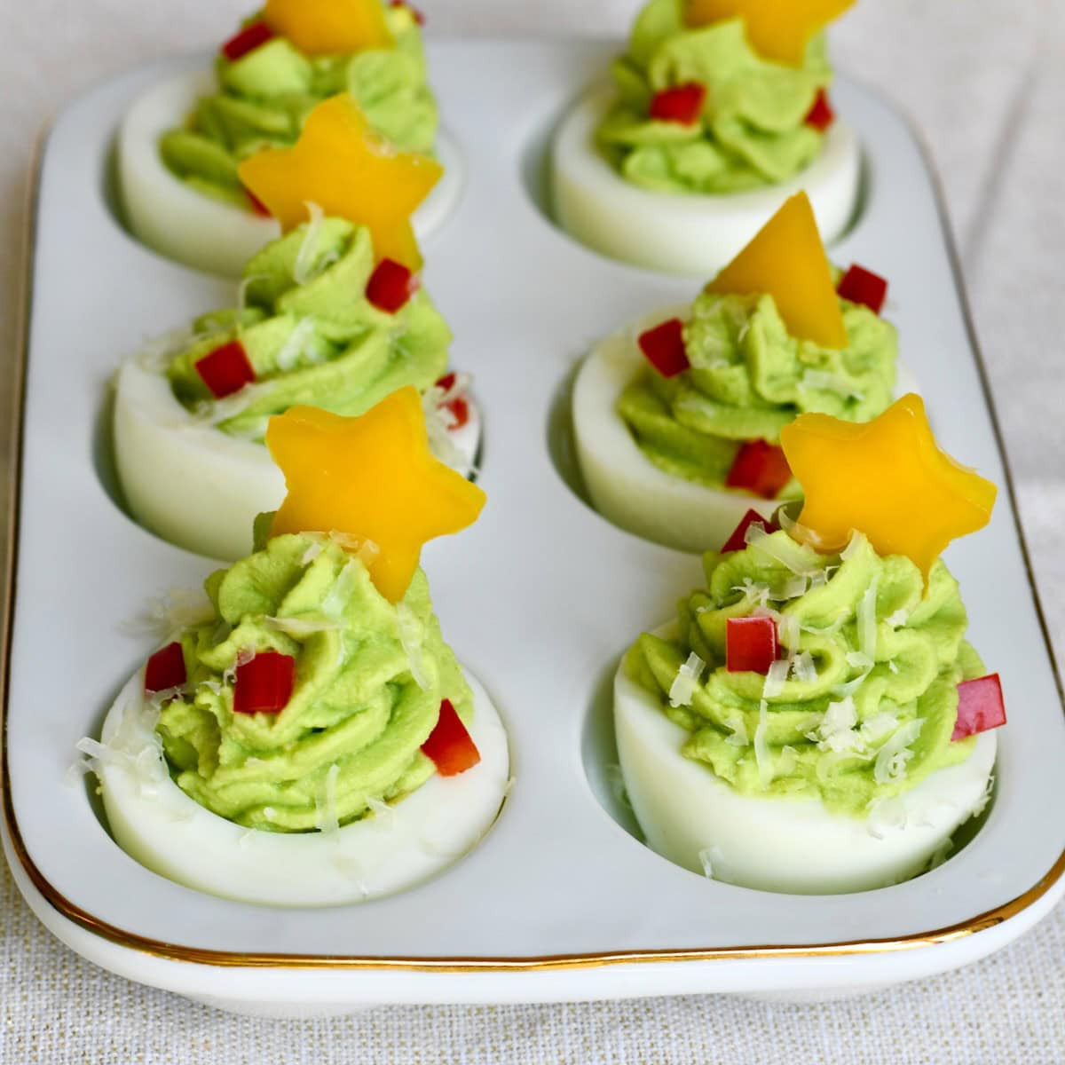 christmas tree deviled eggs topped with yellow bell pepper stars, red pepper ornaments, and parmesan snow