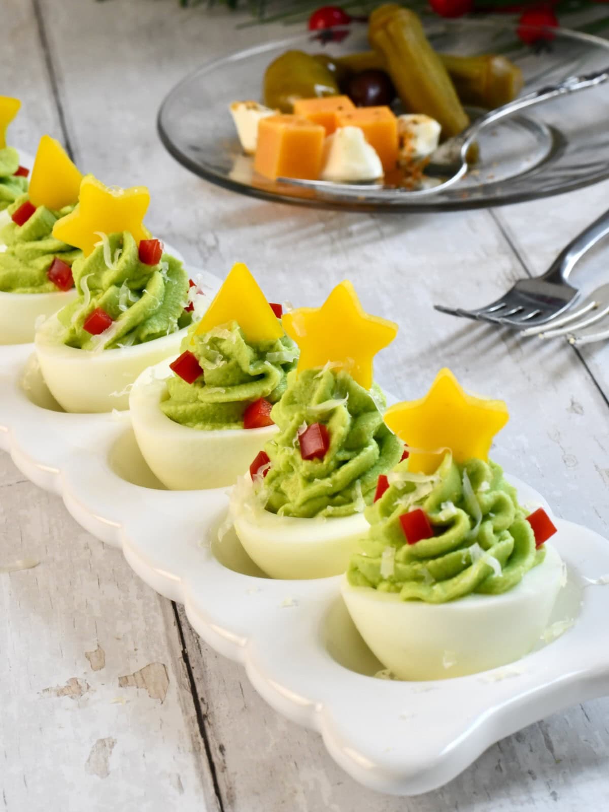 christmas tree deviled eggs decorated with yellow bell pepper stars on top, arranged in a white serving dish