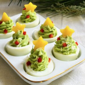 christmas tree deviled eggs decorated with yellow bell pepper stars, red pepper ornaments, and parmesan snow
