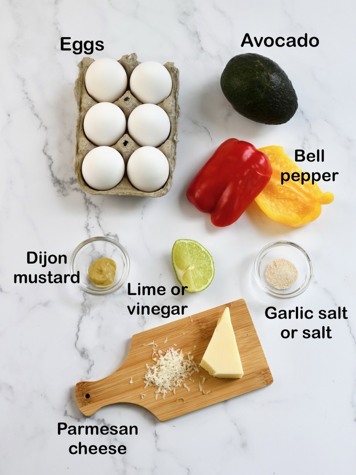 ingredients for christmas tree deviled eggs including eggs, avocado, red and yellow bell peppers, dijon mustard, lime, garlic salt, and parmesan cheese arranged on a marble surface