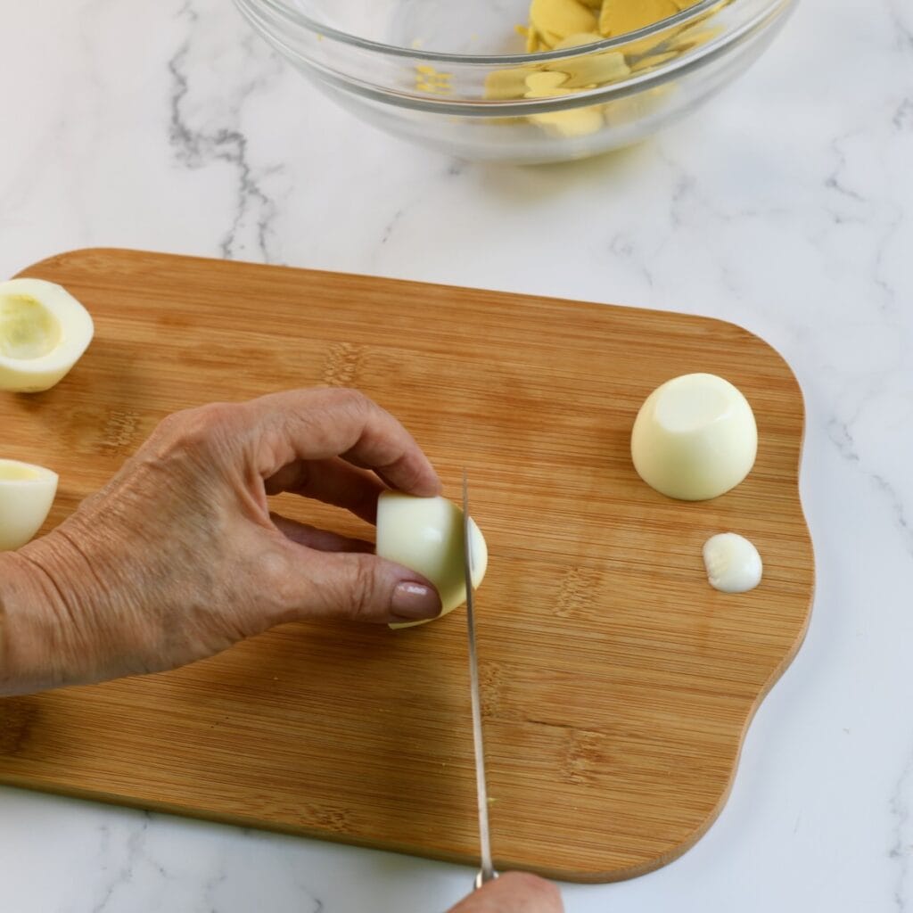 Crosswise-cut hard-boiled eggs with yolks removed, arranged on a cutting board beside a knife and a bowl of yolks