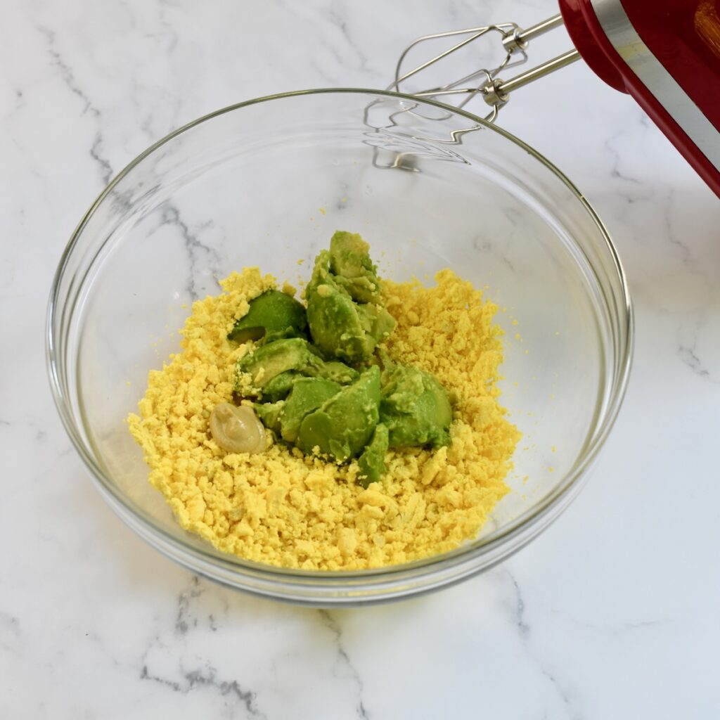 Glass mixing bowl with mashed egg yolks and ripe avocado, ready to be blended for deviled egg filling