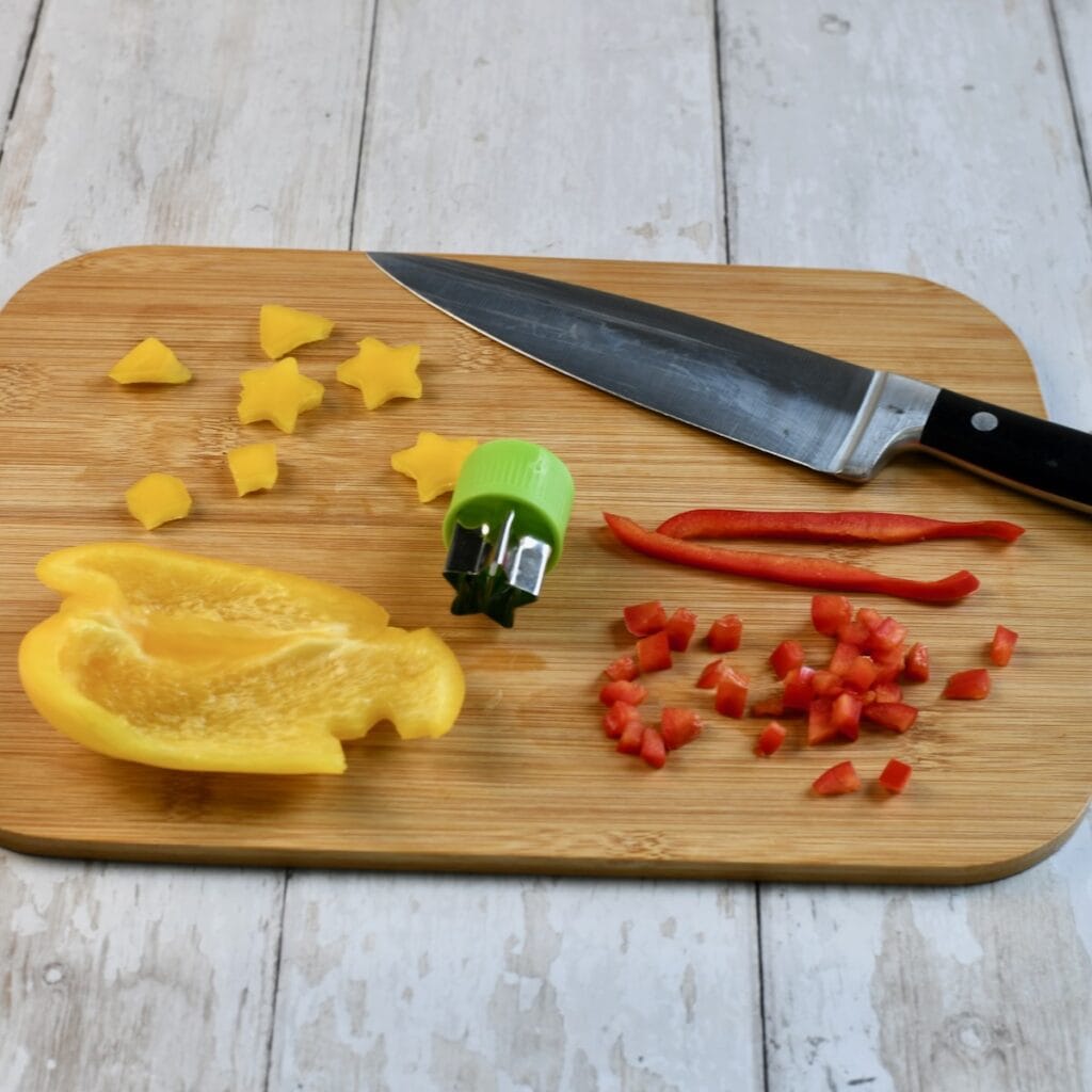 cutting board with diced red bell pepper, yellow pepper stars, and a knife for decorating christmas tree deviled eggs