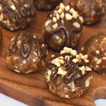 Pecan pie balls on a wooden board, some topped with chocolate drizzle and others sprinkled with chopped pecans