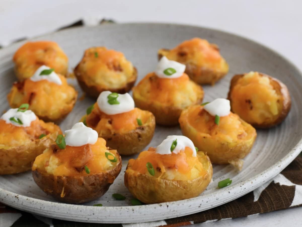 Mini twice baked potatoes on a gray serving plate, topped with sour cream and chopped chives