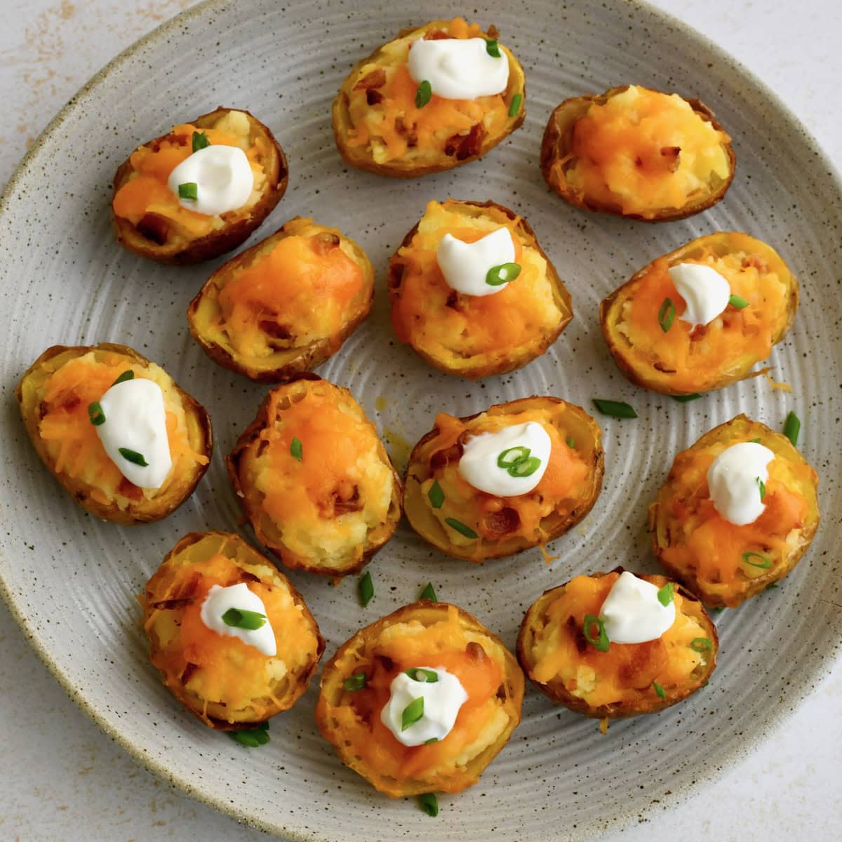 Mini twice baked potatoes arranged on a plate, topped with sour cream and sliced green onions