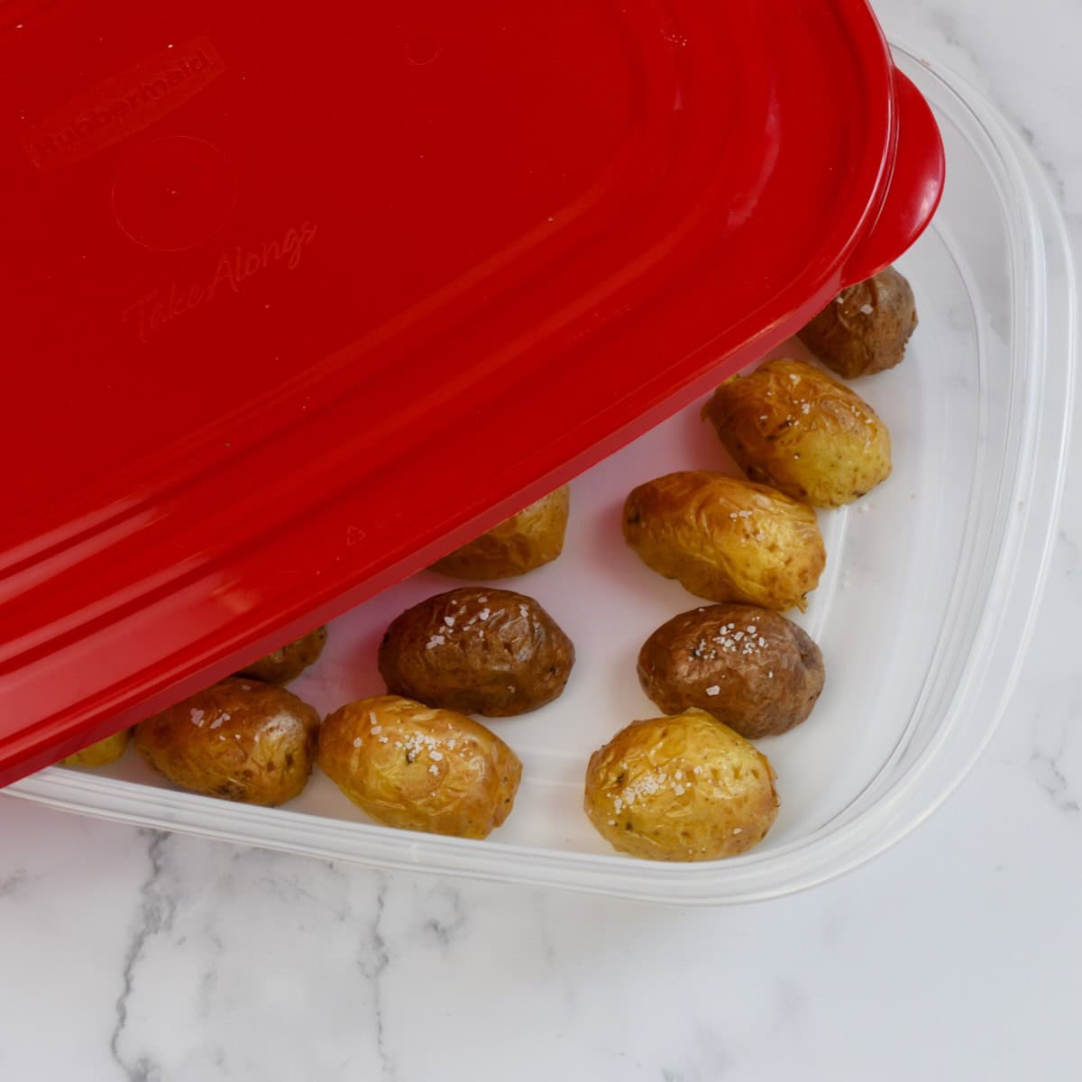 Cooked mini potatoes stored in a plastic container with a red lid