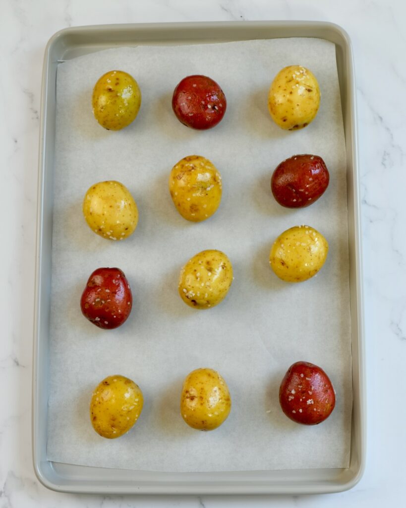 Uncooked potatoes arranged on a baking sheet 
