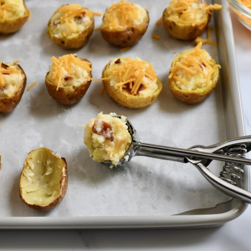 Scooping creamy potato filling into hollowed potato skins on a parchment-lined baking sheet 
