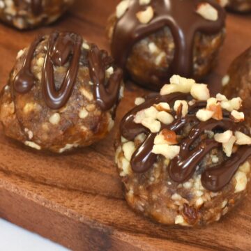Close-up of pecan pie balls on a wooden board, topped with chocolate drizzle and chopped pecans
