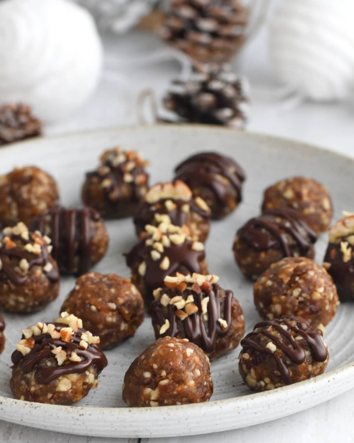 Pecan pie balls on a white plate, decorated with chocolate drizzle and chopped pecans