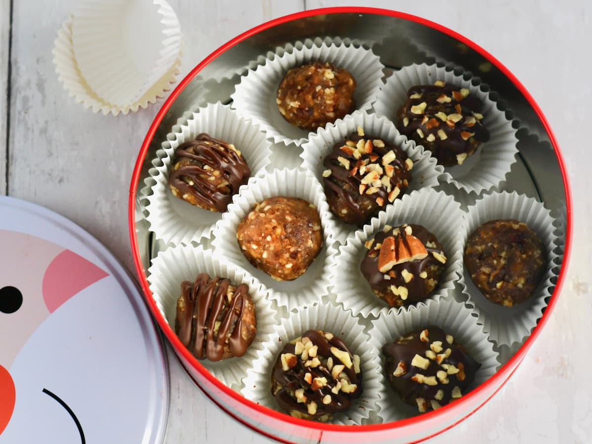 Chocolate-covered pecan pie balls in white paper liners, arranged inside a red holiday tin