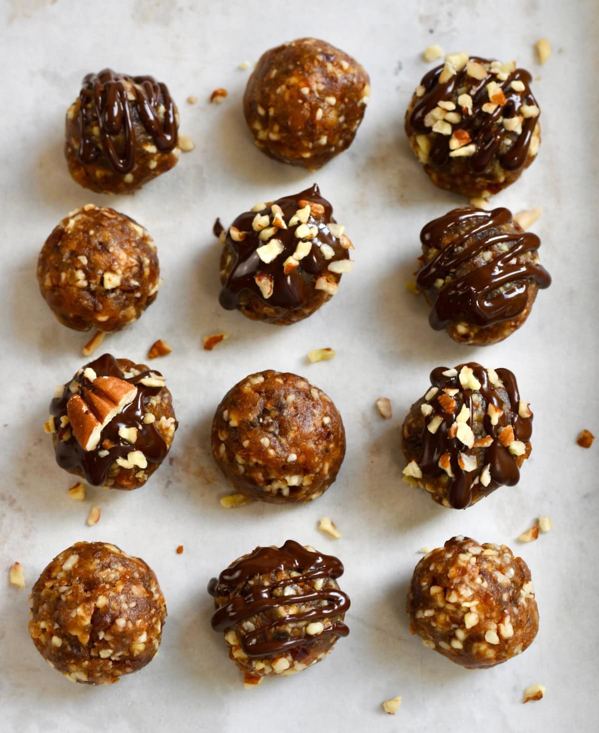 Pecan pie balls on parchment paper, some drizzled with chocolate and topped with chopped pecans