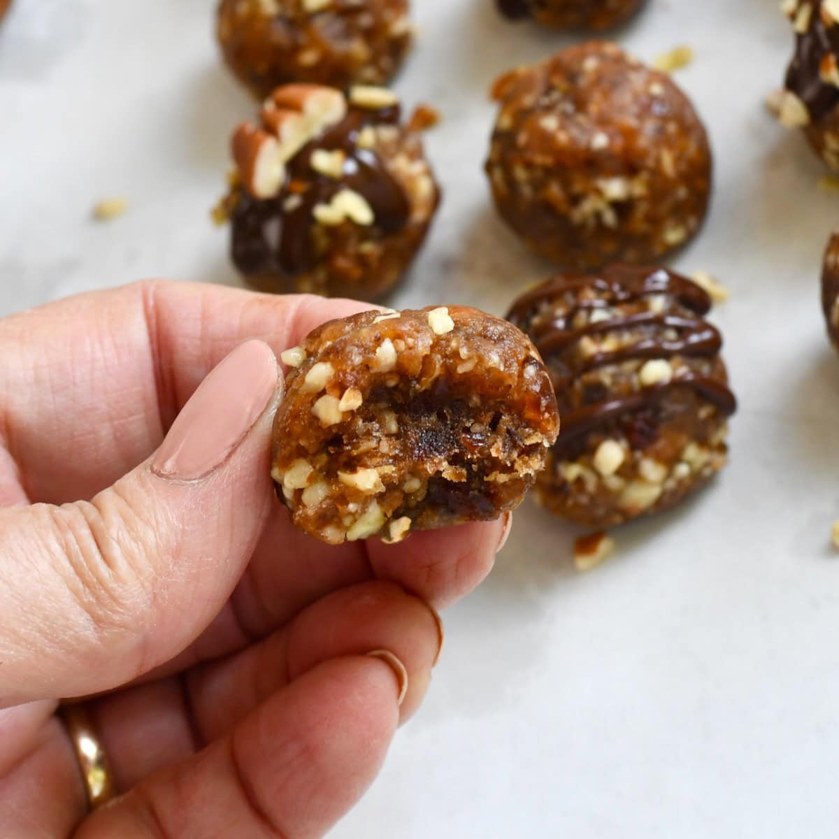 Hand holding a pecan pie ball with a bite taken out, showing the chewy date and pecan filling inside