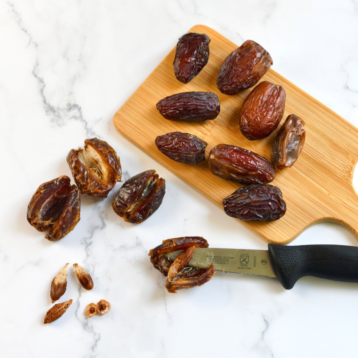 Medjool dates on a small wooden cutting board with a knife, some sliced open to show the pits removed