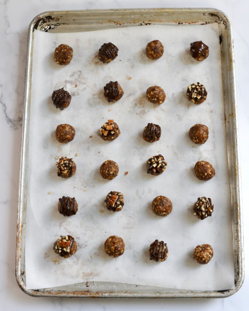 Rolled pecan date mixture shaped into balls and arranged on a parchment-lined baking sheet