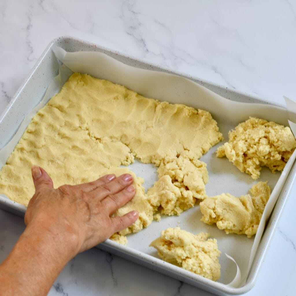 hand pressing sugar cookie dough into a parchment-lined baking pan