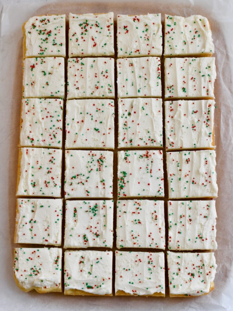 sliced sugar cookie bars with white frosting and red and green sprinkles on parchment paper
