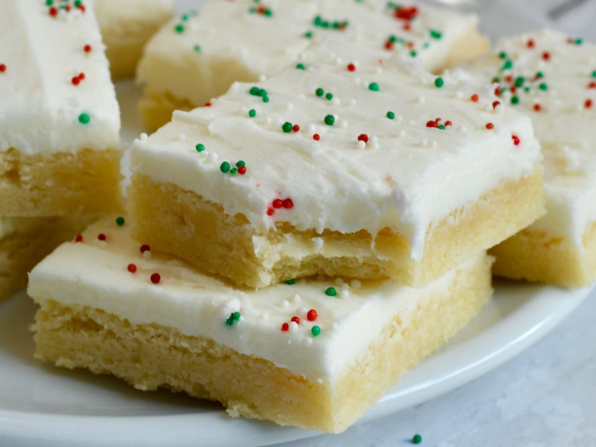 close-up of frosted sugar cookie bar squares with red and green sprinkles stacked on a plate