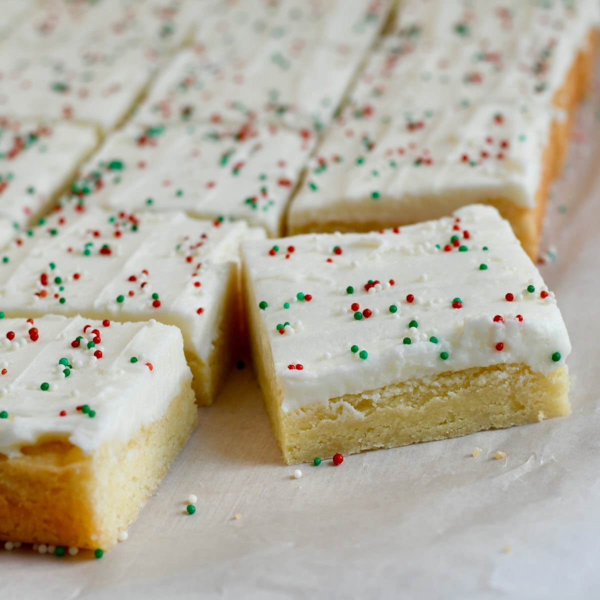 sugar cookie bars cut into even squares, topped with white frosting and holiday sprinkles