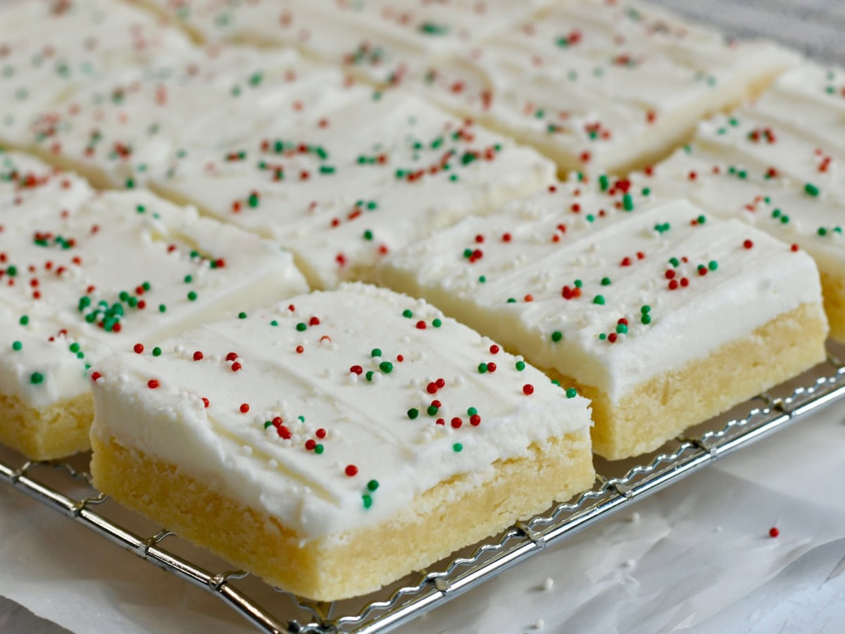 frosted sugar cookie bar squares with red and green sprinkles cooling on a wire rack