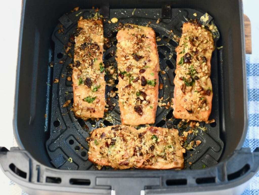 Four pecan-crusted salmon fillets cooked in an air fryer basket until golden brown and crisp