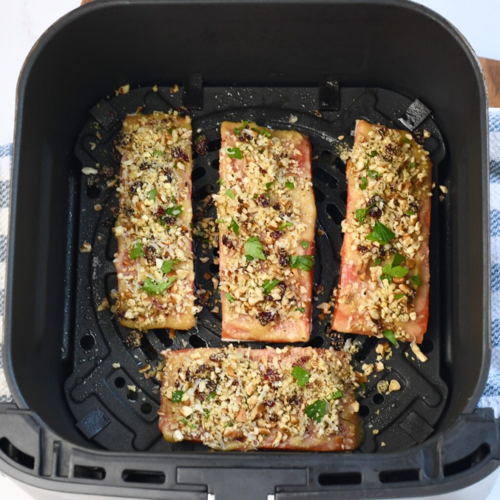 Four salmon fillets topped with a pecan, cranberry, and Parmesan crust inside an air fryer basket before cooking