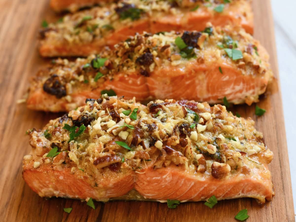 Close-up of baked pecan-crusted salmon fillets topped with golden brown pecans and parsley on a wooden board