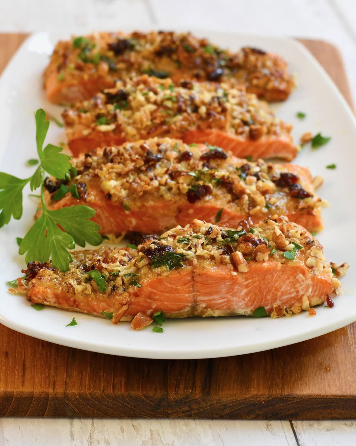 Baked pecan-crusted salmon fillets arranged on a white serving plate and garnished with fresh parsley