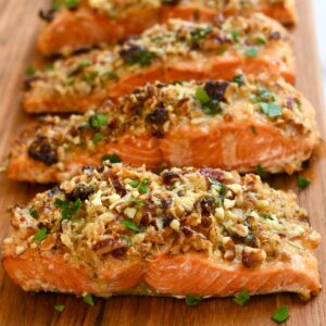 Close-up of pecan-crusted salmon fillets topped with golden brown nuts and herbs on a wooden serving board