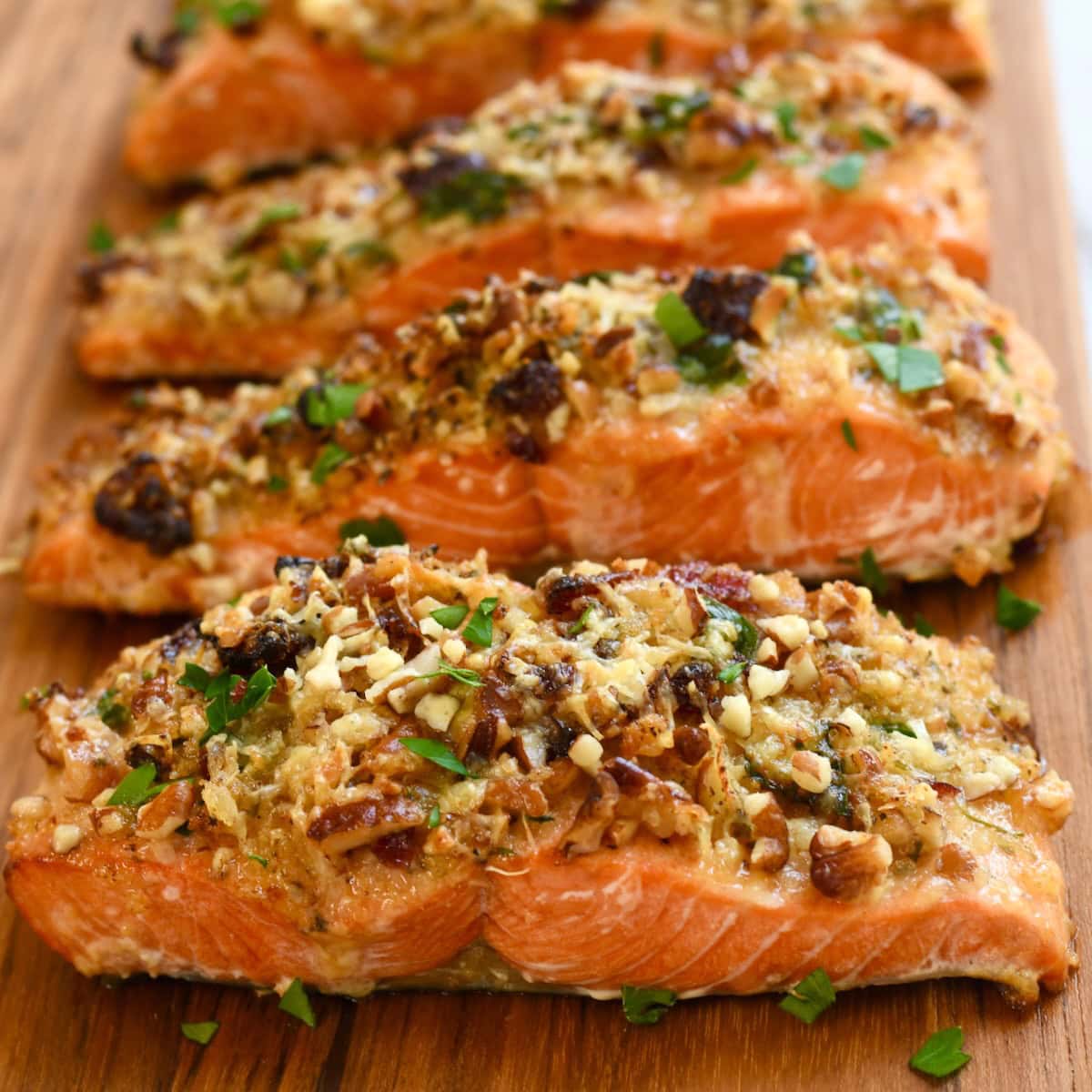 Close-up of pecan-crusted salmon fillets topped with golden brown nuts and herbs on a wooden serving board