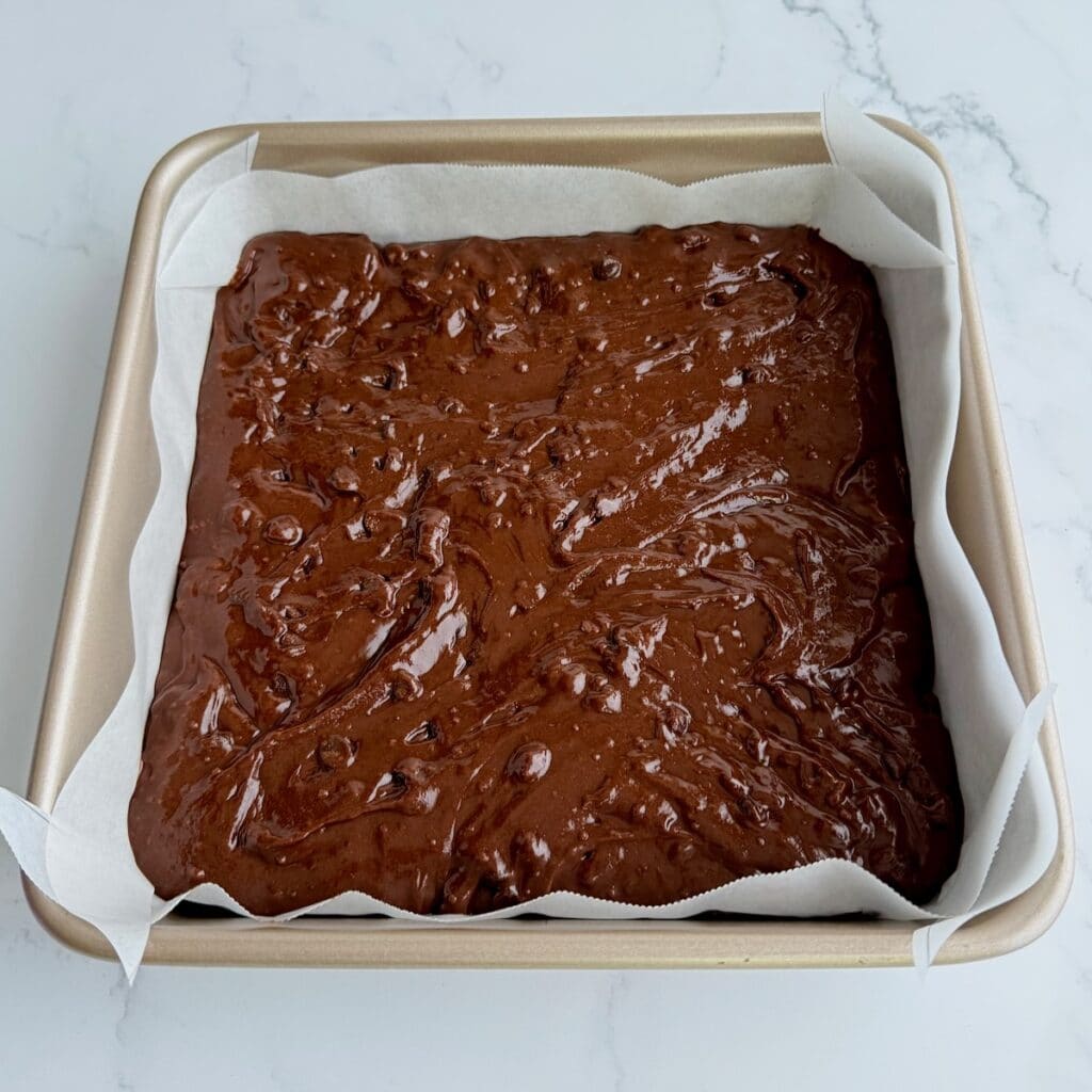 Brownie batter in parchment paper lined pan.