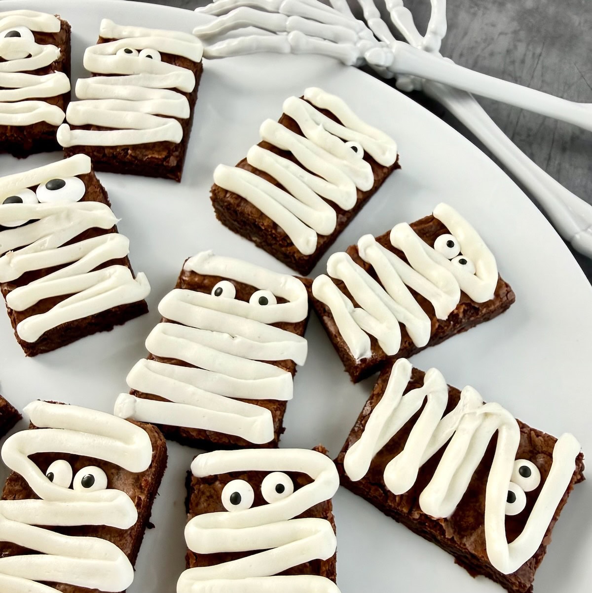 Mummy brownies on white platter with skeleton shaped spoons.