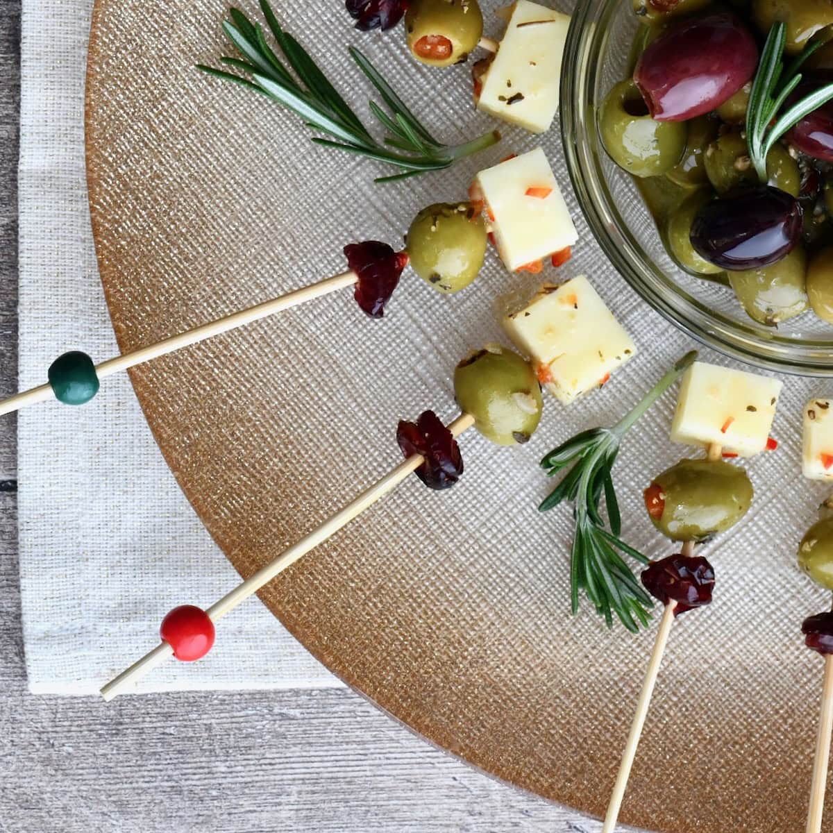 Close-up of Cranberry Olive Cheese Bites arranged on a gold platter with rosemary sprigs