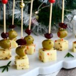 Cranberry Olive Cheese Bites arranged on a white marble platter with rosemary sprigs, set in front of a Christmas tree background