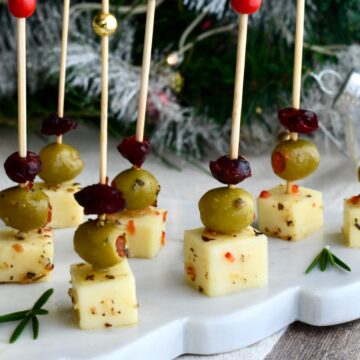 Cranberry Olive Cheese Bites arranged on a white marble platter with rosemary sprigs, set in front of a Christmas tree background