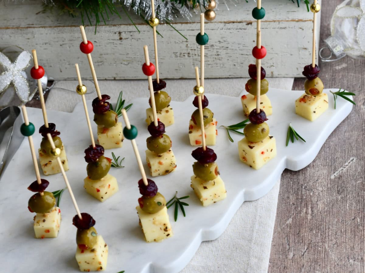 Cranberry Olive Cheese Bites arranged neatly on a white scalloped marble platter with rosemary sprigs